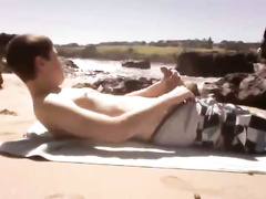 A lone surfer plays with his dick on a beach